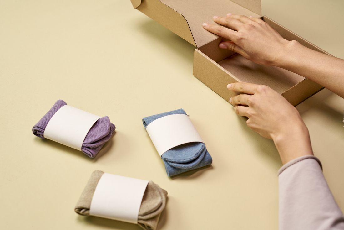 Folded merchandise beside hands preparing an open cardboard box